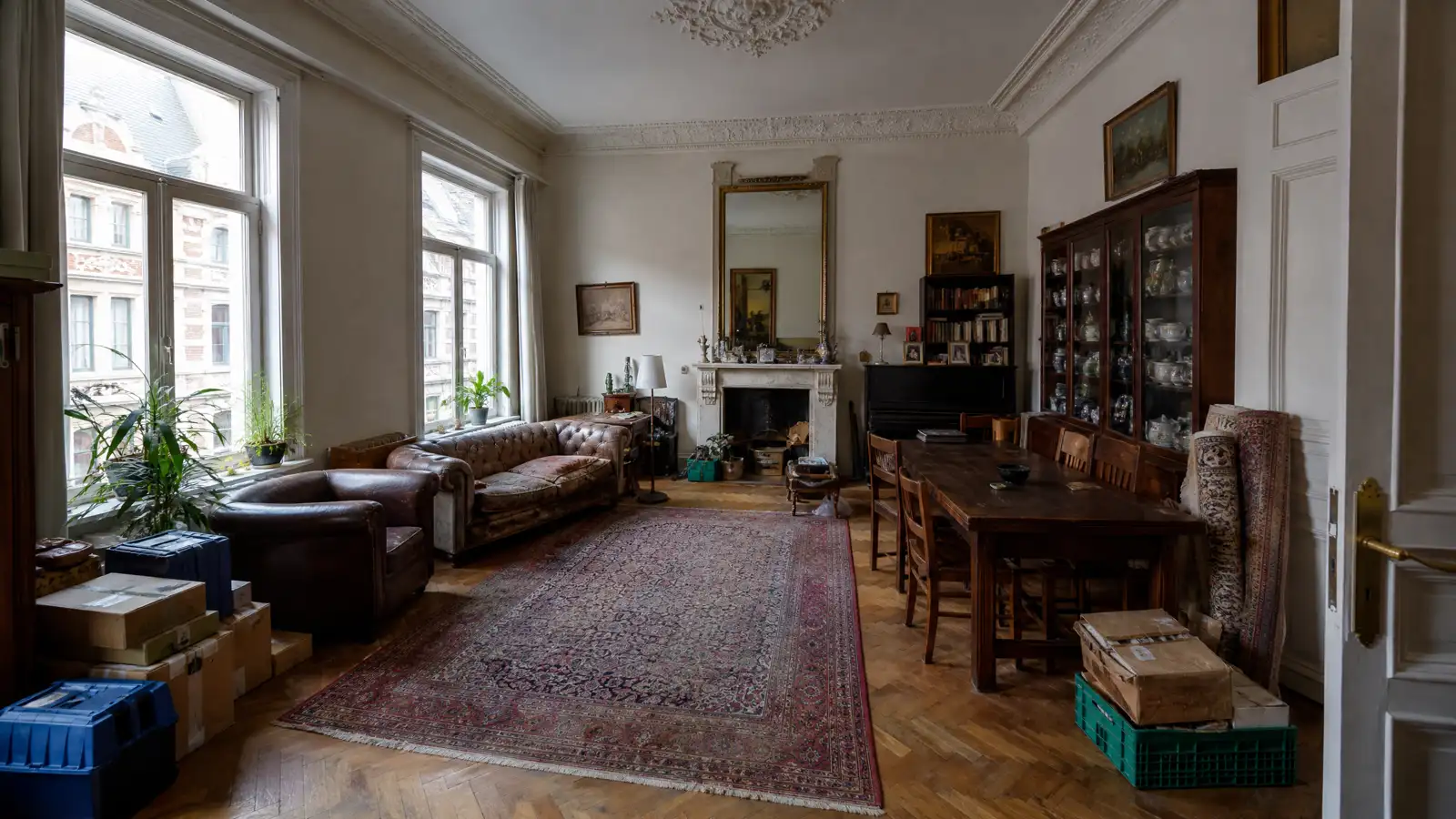 Full living room of an Antwerpen belle-epoque apartment with a chesterfield sofa, a piano, a china cabinet and boxes, just before a house clearance