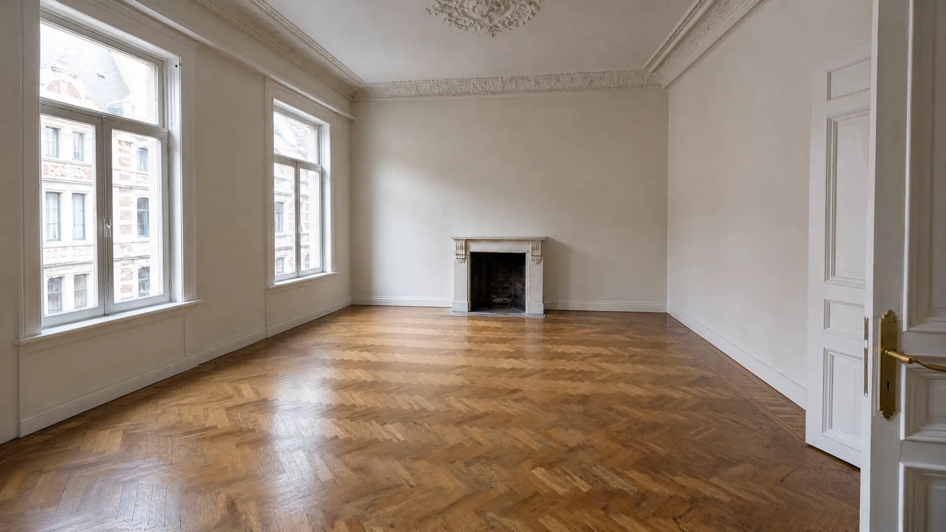 The same Antwerpen living room after the house clearance: empty, swept herringbone parquet and a marble fireplace