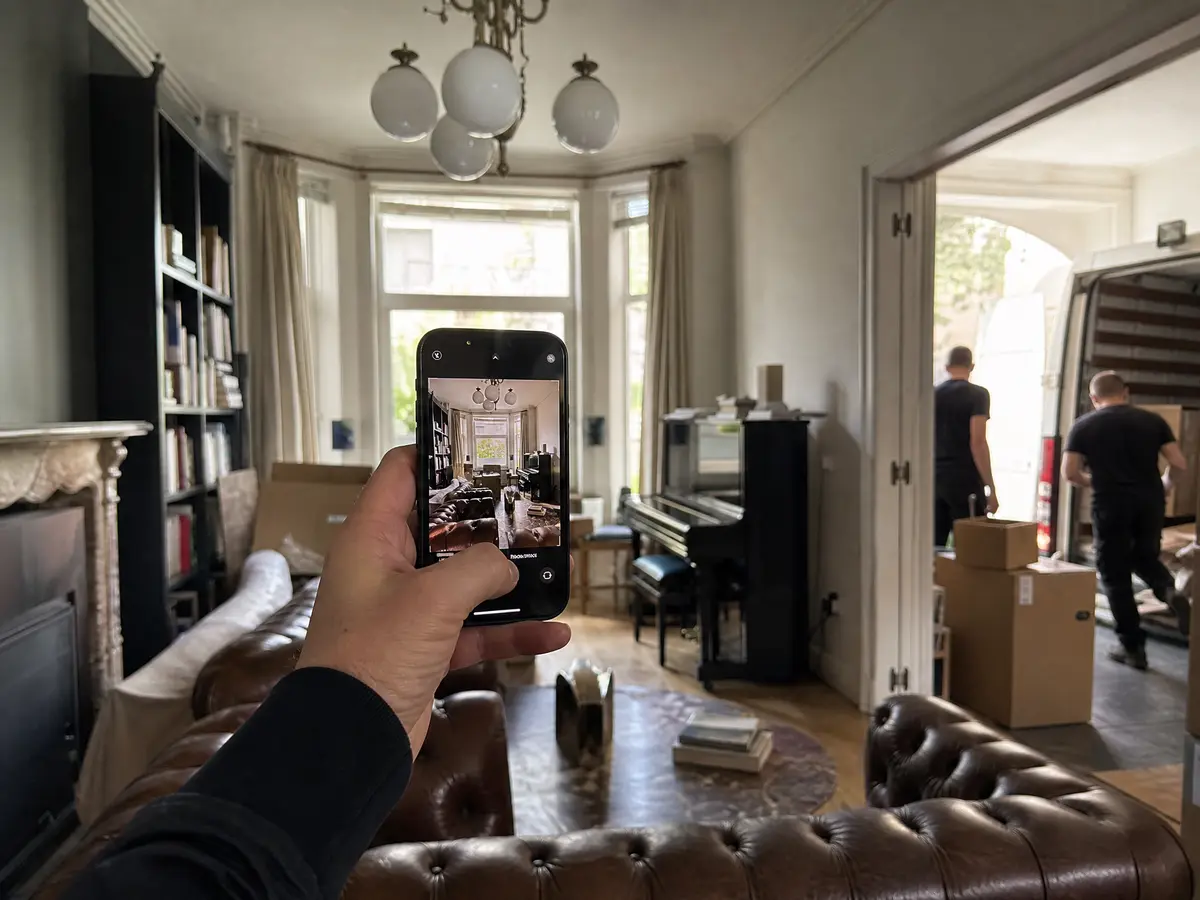 A hand photographs a crowded Antwerpen living room with a smartphone to ask for a house clearance price