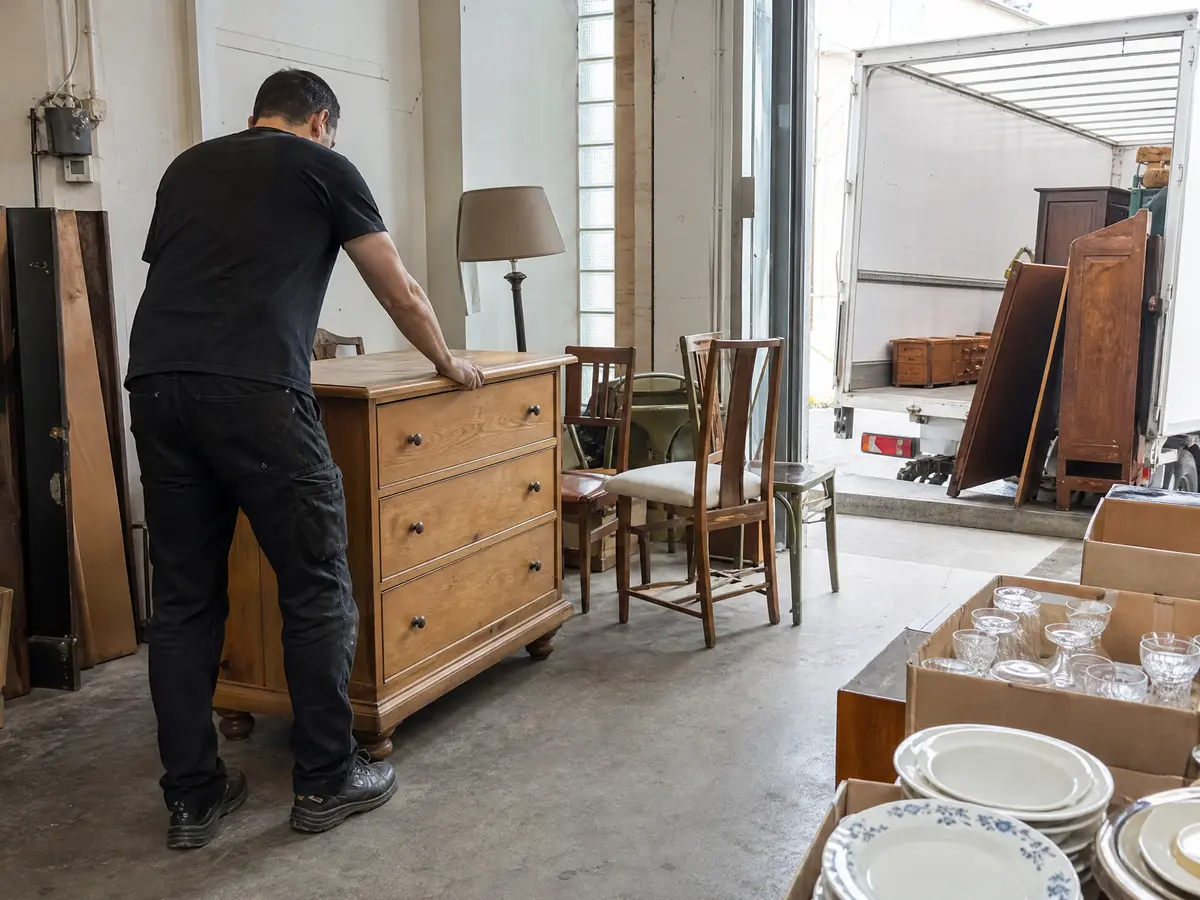 Crew member sets down a good oak chest of drawers in a second-hand shop after a house clearance in Antwerpen